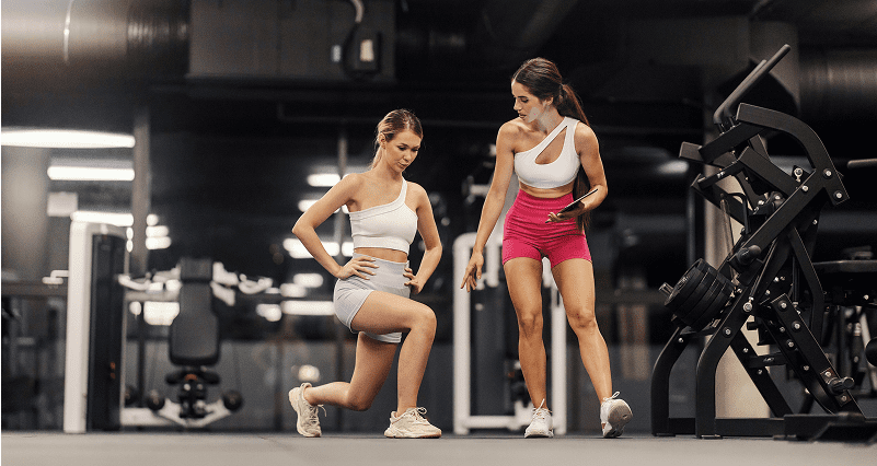 Two women stretching before exercise in a gym.