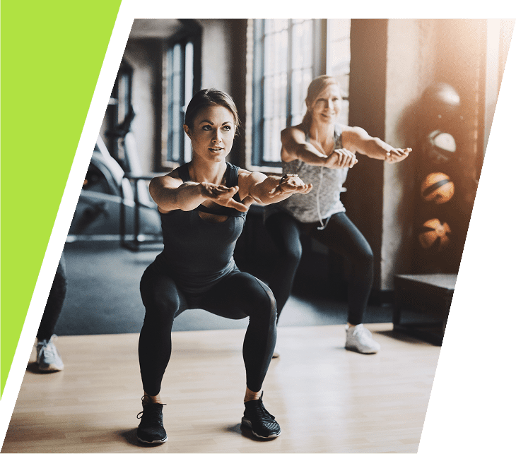 Two women exercising indoors, doing squats with arms extended.