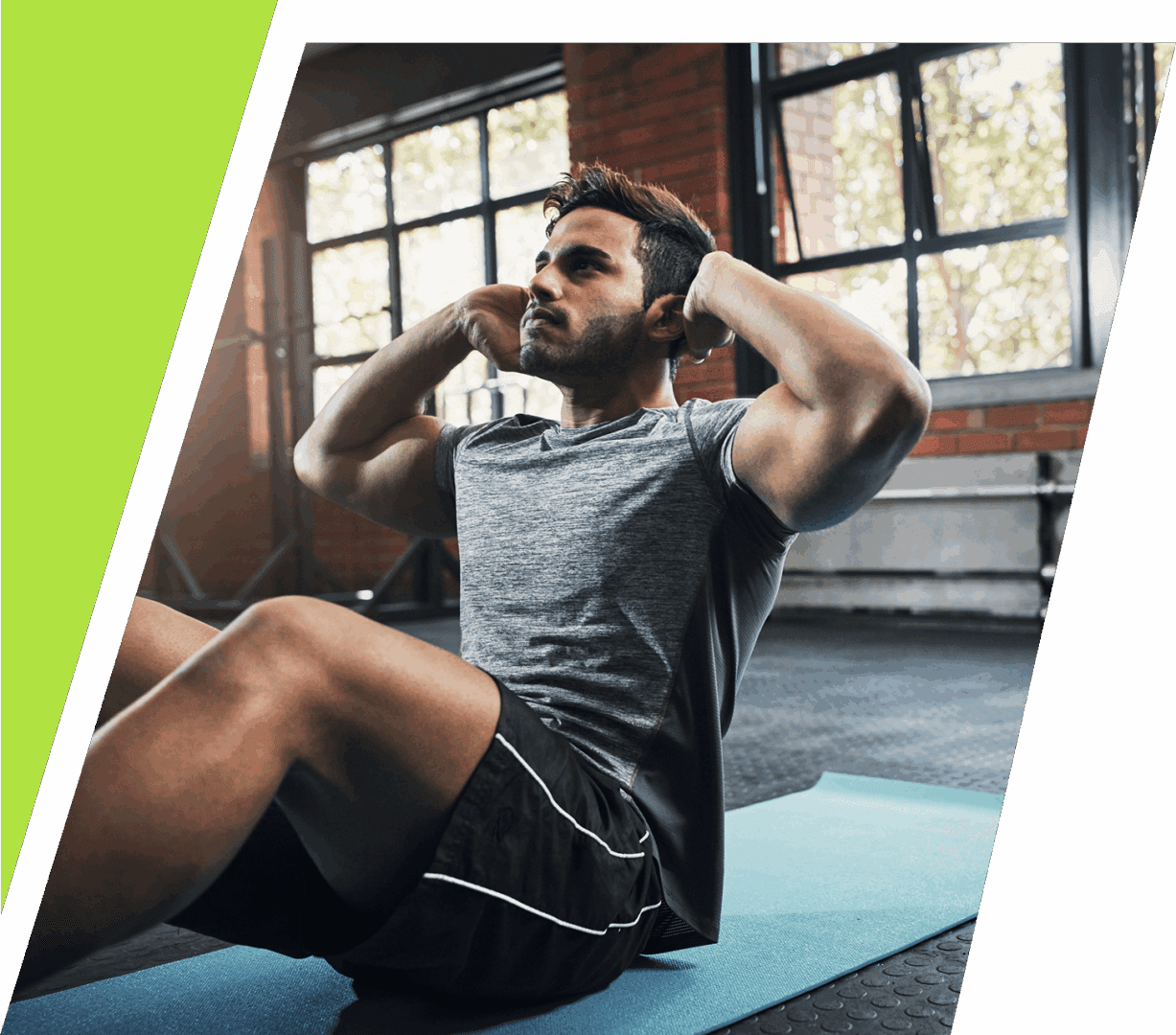 A man doing sit-ups on a mat in a gym with large windows.