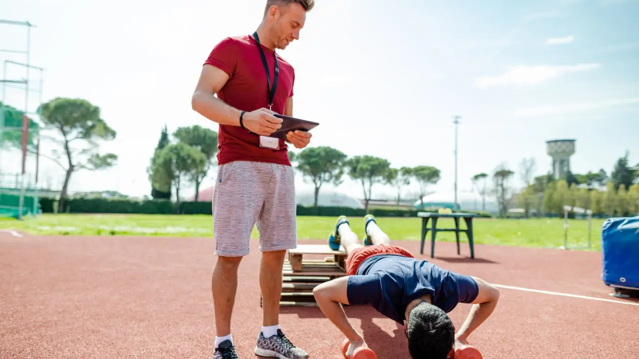 A man doing push-ups outdoors while another watches.