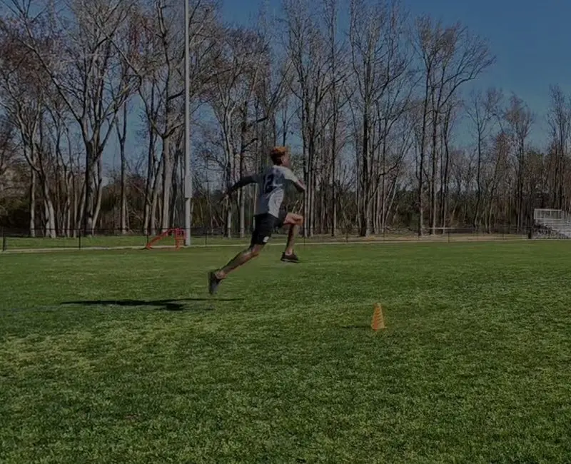 A person running on a grassy field with cones.