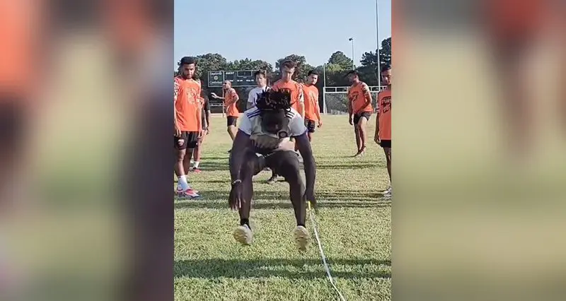 A person carrying another during a sports practice on a grassy field.