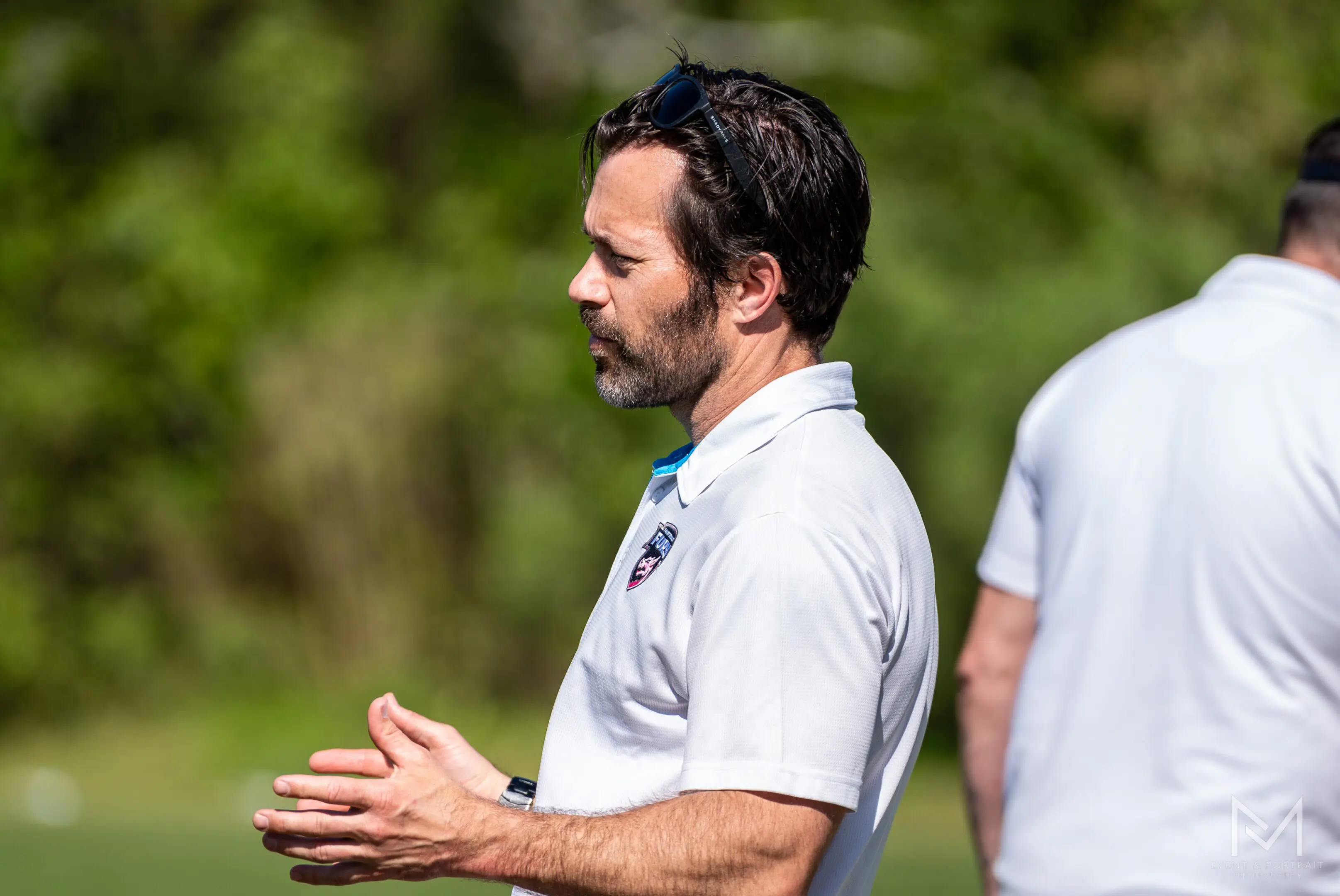 Man in white polo shirt gesturing outdoors.