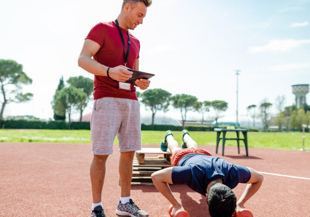 A man doing push-ups outdoors while another watches.